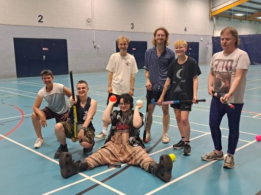  A group of people some standing up and others sitting down, holding hockey sticks and hockey balls.