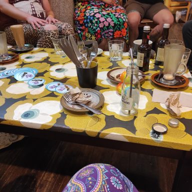 People sitting around a  table with cups, plates and glass bottles  