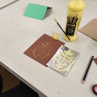 a bottle of yellow paint, a paint brush, a piece of brown card with a pattern that has been printed on